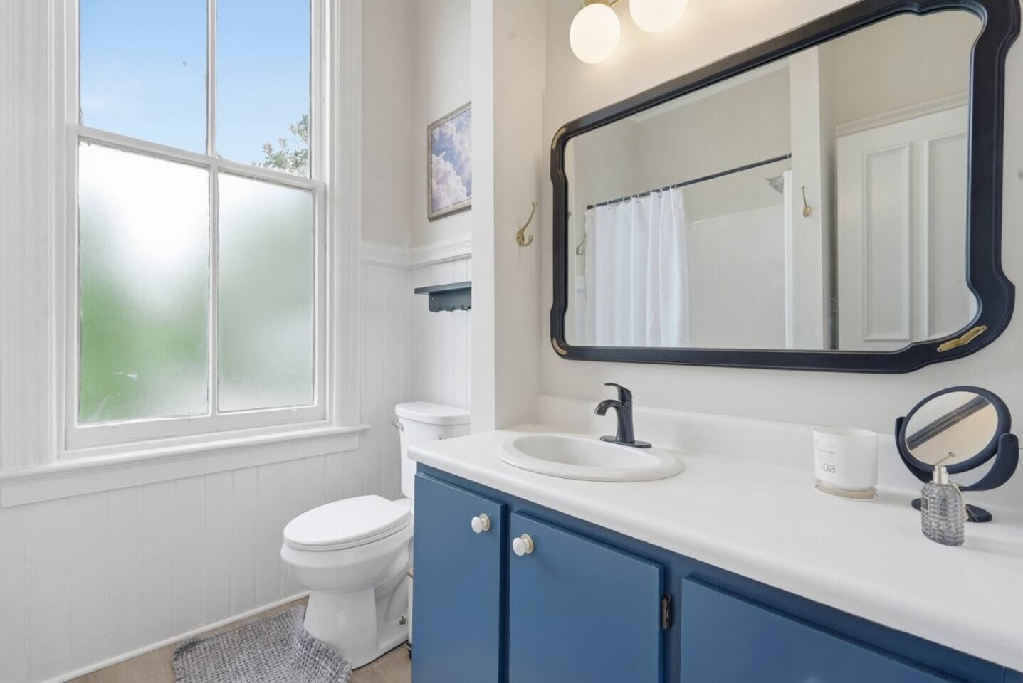 Une salle de bain avec des toilettes blanches, un meuble-lavabo bleu avec un évier blanc et un grand miroir au-dessus du meuble-lavabo.