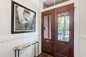 A hallway with a wooden door, a framed picture on the wall, and a small table with magazines. - Stylish Downtown Savannah Stay (Savannah)