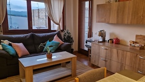 Ein gemütlicher Wohnbereich mit einer Couch, einem Couchtisch und Blick auf ein Gebäude durch ein Fenster.