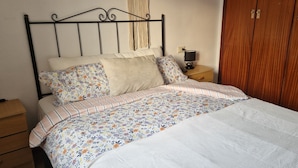 Ein Bett mit Blumenmuster auf der Bettwäsche, ein Nachttisch mit Lampe und ein Holzschrank.