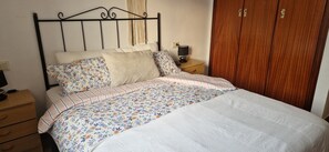 A bed with floral bedding, a bedside table with a lamp, and a wooden wardrobe. - La Ampolla by the Sea (L'Ampolla)