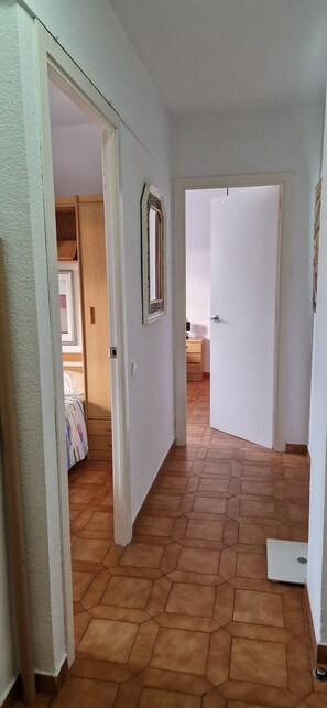 A hallway with a tiled floor, white walls, and a door leading to a bedroom with a bed and a dresser. - La Ampolla by the Sea (L'Ampolla)