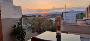A balcony with a table and chairs, overlooking a cityscape with buildings and a sunset. - La Ampolla by the Sea (L'Ampolla)