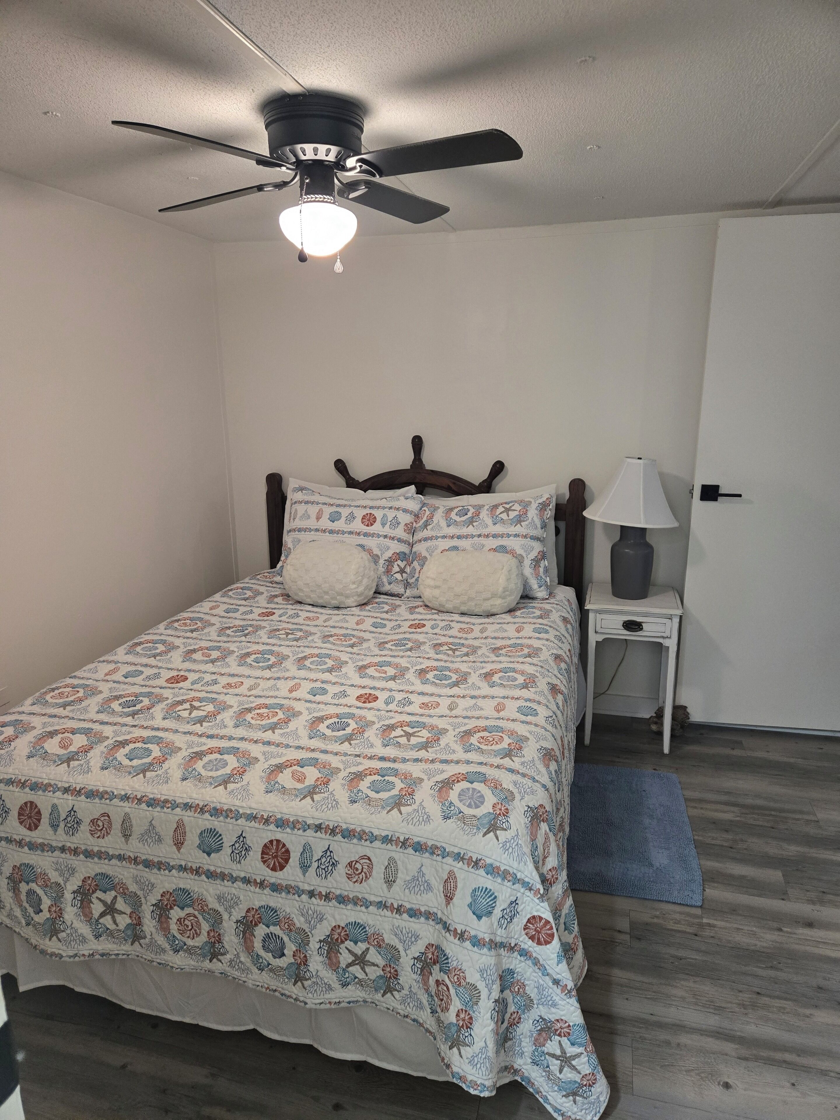 A bedroom with a bed, a ceiling fan, a bedside lamp, and a door.