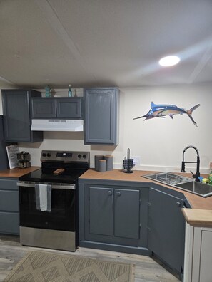Une cuisine avec des meubles gris, une cuisinière noire, un évier avec un robinet noir et un élément décoratif mural représentant des poissons.