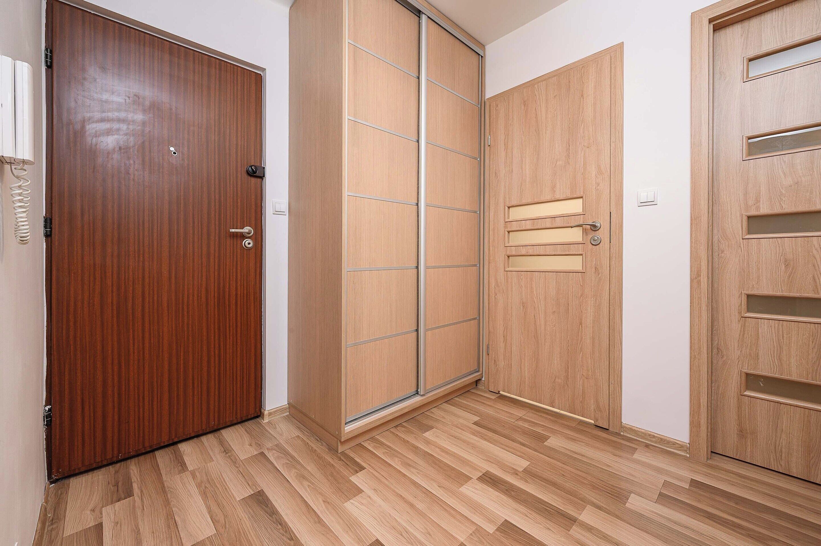 A room with a wooden door, a sliding closet door, and a solid door with a handle.