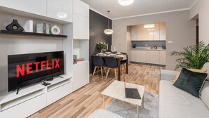 A modern living room with a flat-screen TV displaying 'NETFLIX,' a dining area with a table set for two, and a kitchen with light wood cabinets. - 2-bed Home on Krochmalna (Warsaw)