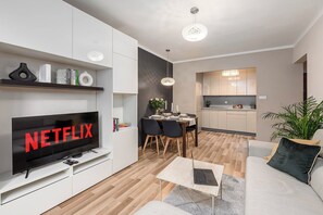 A modern living room with a flat-screen TV displaying 'NETFLIX,' a dining area with a table set for two, and a kitchen with light wood cabinets. - 2-bed Home on Krochmalna (Warsaw)