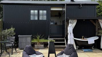 A black metal building with a small window and a door, a black bathtub, and two bean bag chairs on a gravel area.