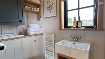 A bathroom with a toilet, a sink, a window, and a shelf with towels.