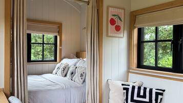 A bedroom with a bed, bench, windows, and a wall-mounted picture.