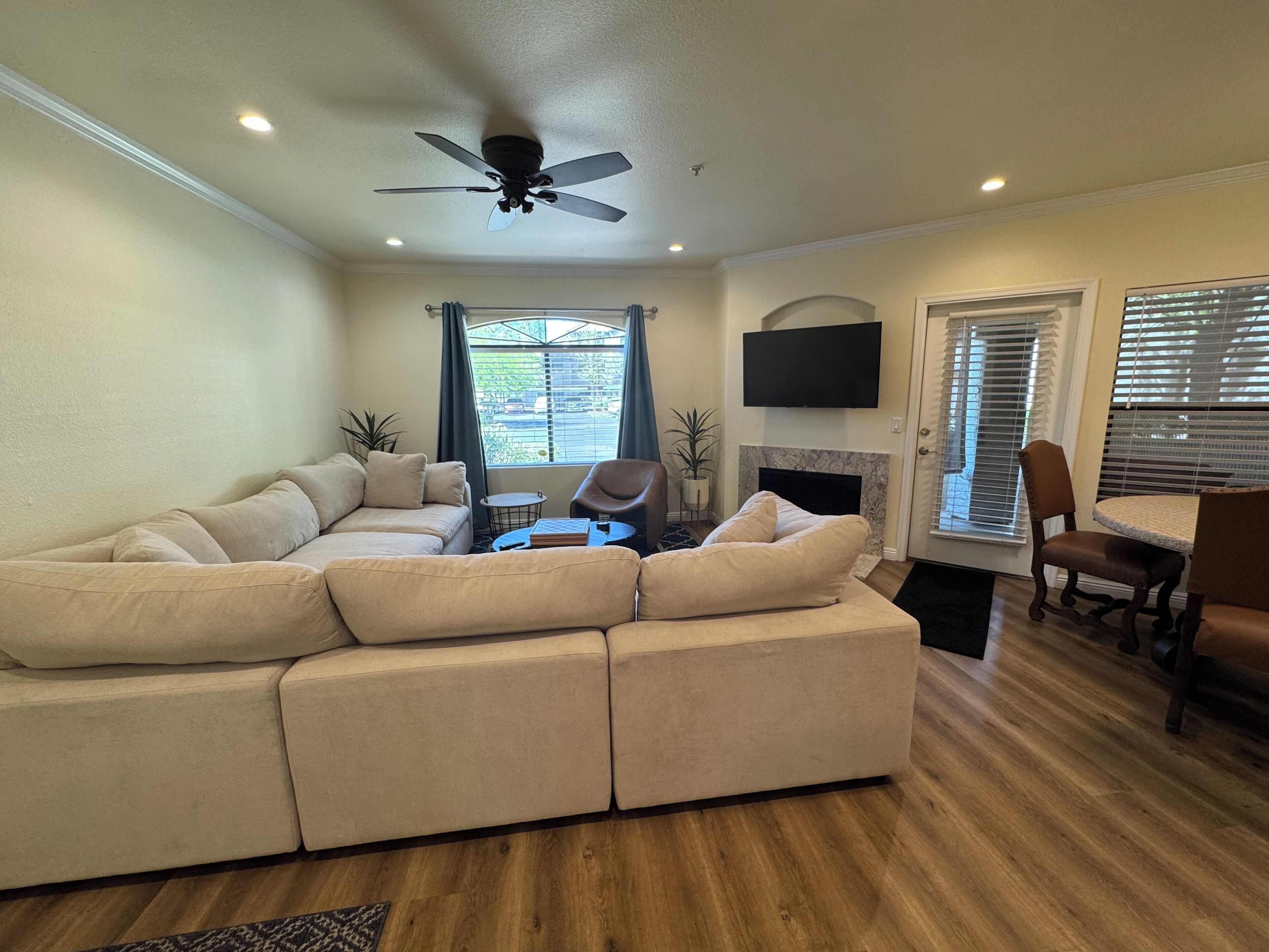 A living room with a sectional sofa, a fireplace, a dining area with a table and chairs, and a ceiling fan.