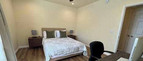 A bedroom with a bed, bedside tables, a desk with a chair, a computer, and a ceiling fan.