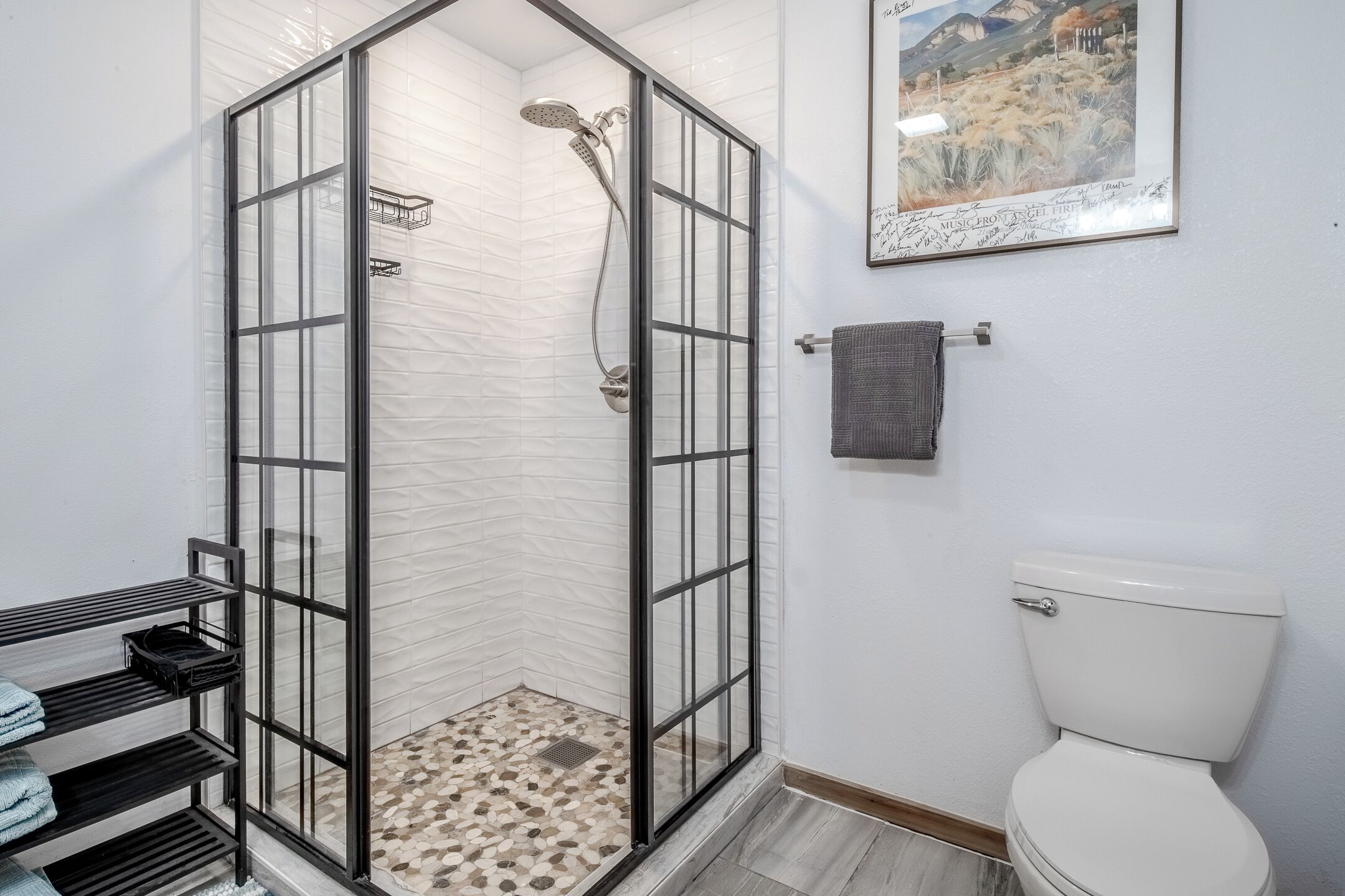 Een badkamer met een douchecabine van glas, een toilet, een handdoekrek en een plank met handdoeken.