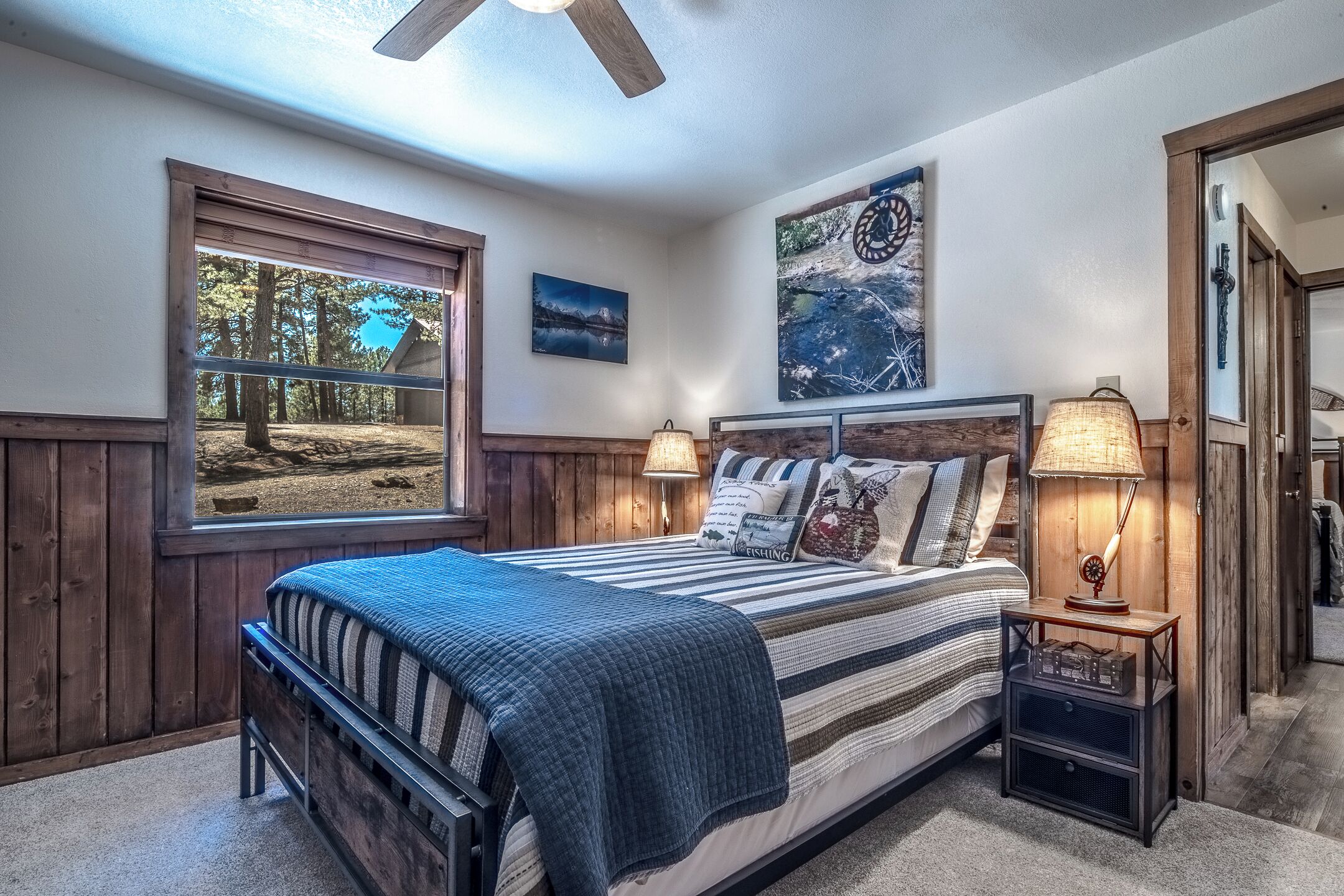 A bedroom with a large window, a bed with striped bedding, two bedside lamps, and a ceiling fan.