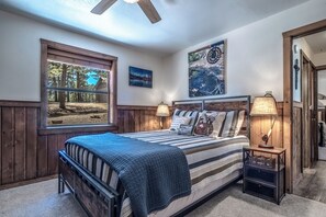 Een slaapkamer met een groot raam, een bed met gestreepte lakens, twee bedlampen en een plafondventilator.