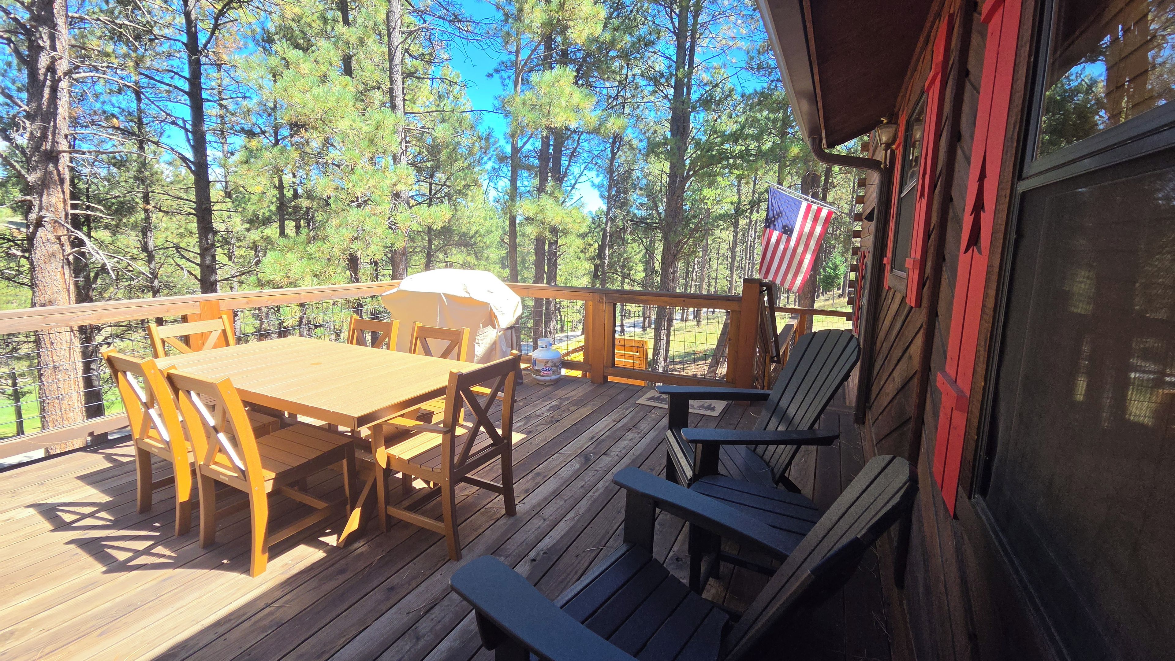 A wooden deck with a table and chairs, an American flag, and a grill.