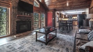 Ein großzügiges Wohnzimmer mit Kamin aus Stein, ein Essbereich mit Holztisch und -stühlen sowie eine Küche mit modernen Geräten.