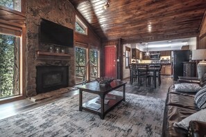 Ein großzügiges Wohnzimmer mit Kamin aus Stein, ein Essbereich mit Holztisch und -stühlen sowie eine Küche mit modernen Geräten.
