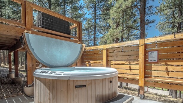 Ein Whirlpool mit Holzverkleidung, einem Metalldeckel und einer umlaufenden Holzterrasse.