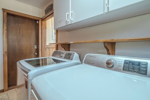 Ein Waschraum mit zwei weißen Frontlader-Waschmaschinen, Holzschränken darüber und einer Holztür.