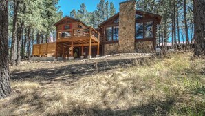 A cabin with a stone chimney, a wooden deck, and a view of the surrounding forest.