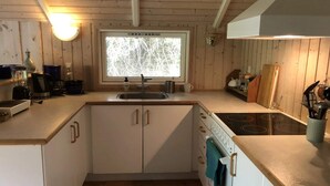 A compact kitchen with wooden cabinets, a built-in oven, a sink, and a window with a view of trees. - 4 Star Holiday Home in Vejby (Vejby)