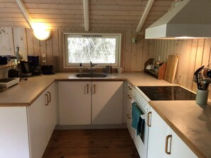 A compact kitchen with wooden cabinets, a built-in oven, a sink, and a window with a view of trees. - 4 Star Holiday Home in Vejby (Vejby)