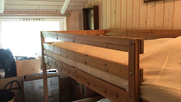 A bunk bed with a wooden frame and white bedding, a window with a view, and a door. - 4 Star Holiday Home in Vejby (Vejby)