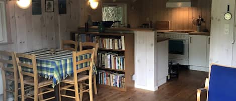 Ein gemütliches Blockhaus-Interieur mit Essbereich, Bücherregal, Küche inklusive Herd und einer Wanduhr.