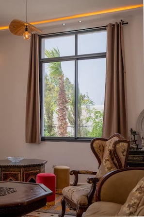 A room with a large window, a chair, a small table, and a hanging light fixture. - Lovely Villa 4 Bedrooms and Swimming pool (Ghazoua)