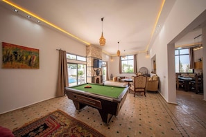 A pool table in a room with a stone wall, a painting, and a dining area with chairs and a table. - Lovely Villa 4 Bedrooms and Swimming pool (Ghazoua)
