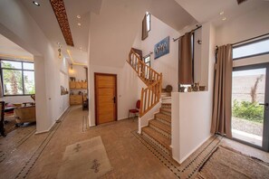 Ein geräumiger Flur, der zu einer Treppe mit hölzernem Geländer, einer Tür mit Verzierungen und einem Durchgang durch eine Glastür führt.