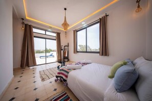A hotel room with a bed, a large window, a ceiling light fixture, and a view of the outside. - Lovely Villa 4 Bedrooms and Swimming pool (Ghazoua)