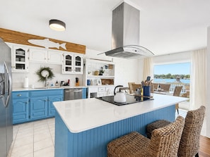 A modern kitchen with a central island, blue cabinetry, and a view of the sea.