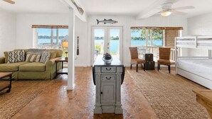 A room with a white ceiling, a wooden floor, a dining table with chairs, a sofa, a bed, and a view of the outdoors. - False River Waterfront Escape in Charming New Roads (New Roads)