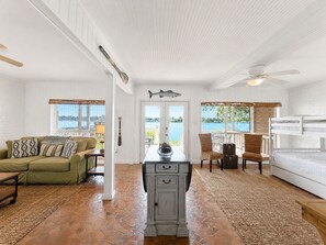 A room with a white ceiling, a wooden floor, a dining table with chairs, a sofa, a bed, and a view of the outdoors. - False River Waterfront Escape in Charming New Roads (New Roads)