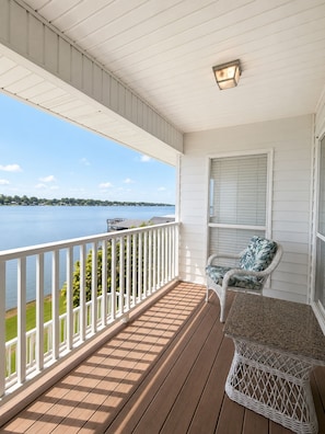 A covered porch with a view of a lake, a wicker chair, and a small table.