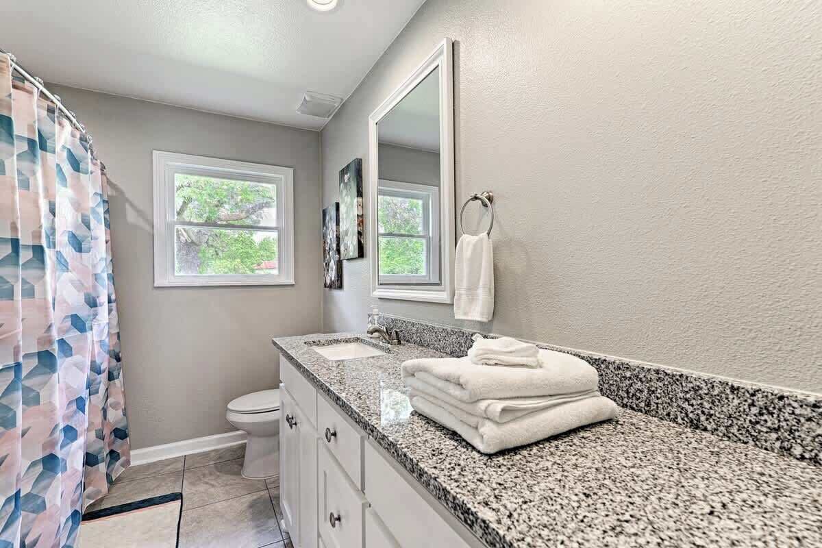 Une salle de bain avec un comptoir en granit, des toilettes, un lavabo, un miroir et un rideau de douche.