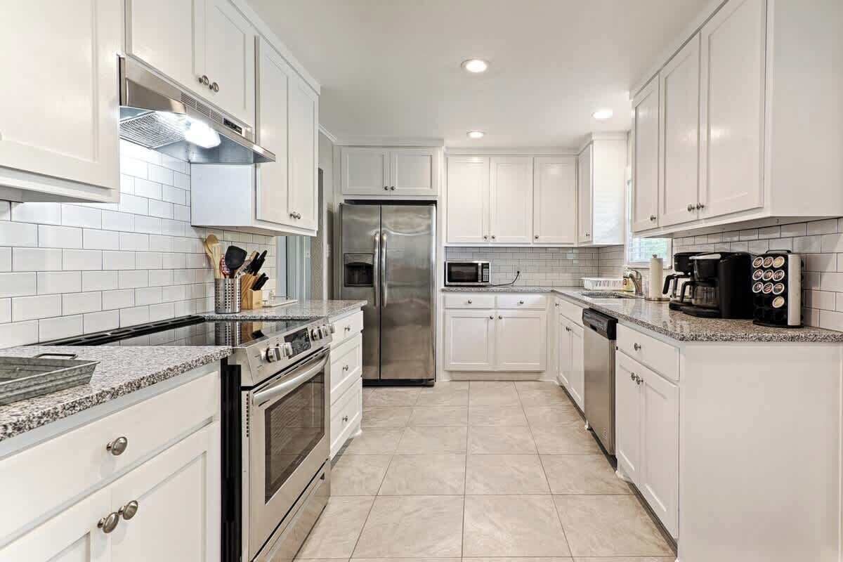 Una cocina moderna con armarios blancos, un refrigerador de acero inoxidable, un microondas y una cafetera.