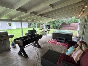A covered outdoor area with a foosball table, barbecue grill, and seating area with cushions. - Hot tub, Game room, Pool, 7 miles to stockyards (Haltom City)