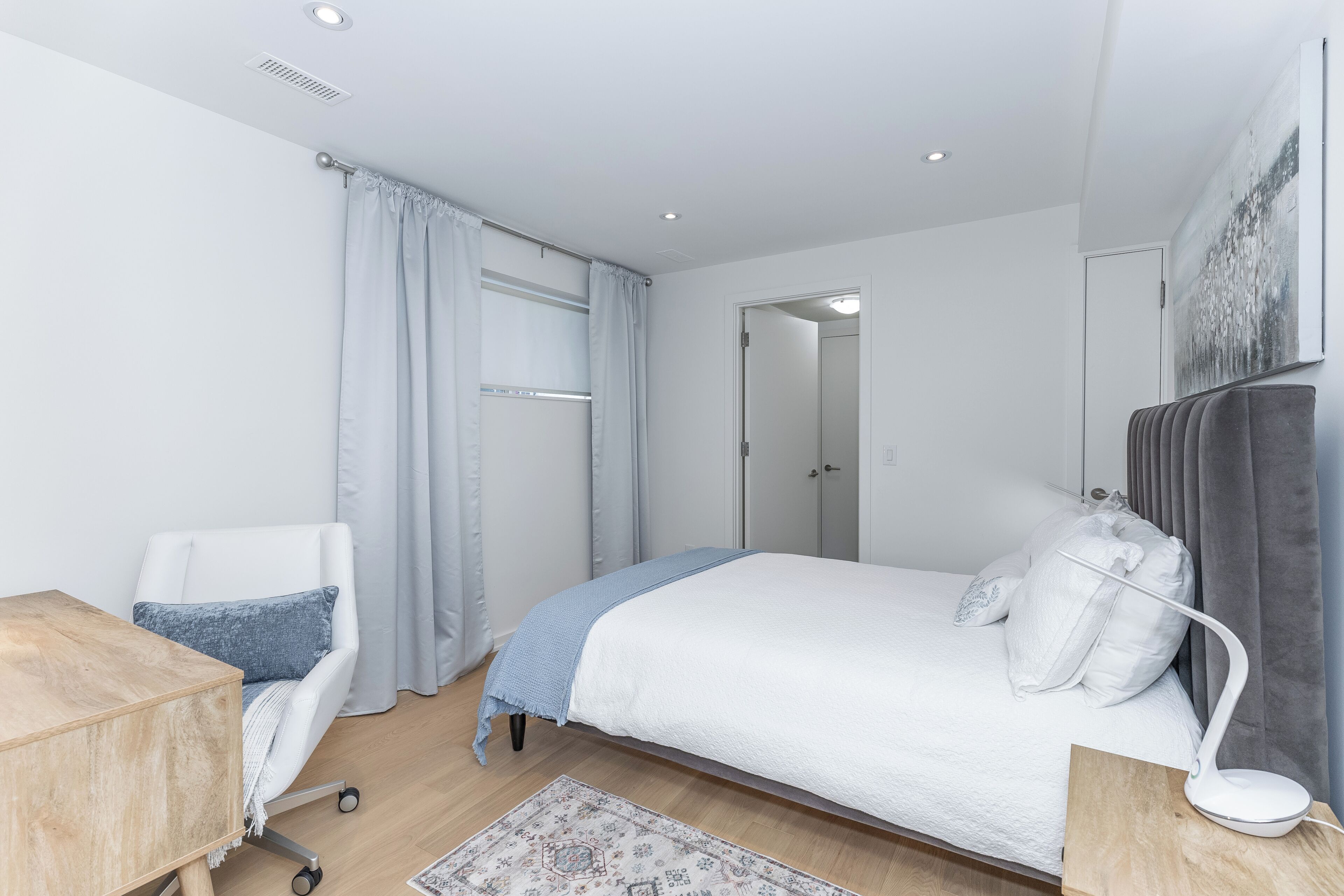A modern bedroom with a bed, a desk, a chair, and a bedside table.