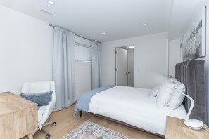 A modern bedroom with a bed, a desk, a chair, and a bedside table.