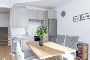 Eine moderne Küche mit Backofen, Kühlschrank und Essbereich mit Holztisch und grau gepolsterten Stühlen.