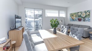 A modern living room with a wooden dining table, grey sofas, and a large window with a view of a snowy outdoor area. -  Bright, Cozy, Separate Entrance, Guest Room, Walk.: Subway, Shop, restaurants.. (Toronto)