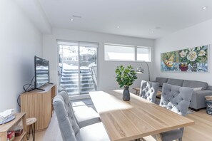 Ein modernes Wohnzimmer mit einem Holzesstisch, grauen Sofas und einem großen Fenster mit Blick auf eine verschneite Landschaft.