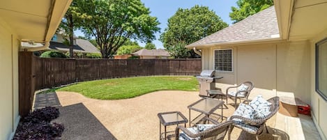 A backyard with a patio area, outdoor furniture, and a grill.