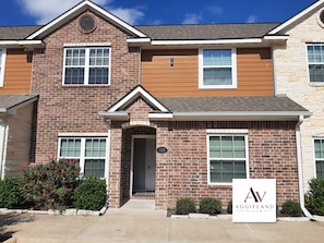 A two-story brick house with a front entrance, a mailbox, and a sign indicating it is part of the Aggieland Villa community. - Aggieland Villa - Themed 4-Bedroom Suite Townhome - Mins to Texas A&M University (College Station)