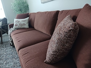 A brown sofa with a patterned pillow and a white pillow with text. - Aggieland Villa - Themed 4-Bedroom Suite Townhome - Mins to Texas A&M University (College Station)