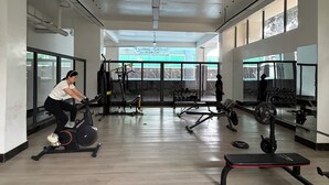 A gym with exercise equipment, a person using an elliptical, and a weight bench. - Cozy & Stylish Apartment with stunning views, 2 minutes from yaya center. (Nairobi)